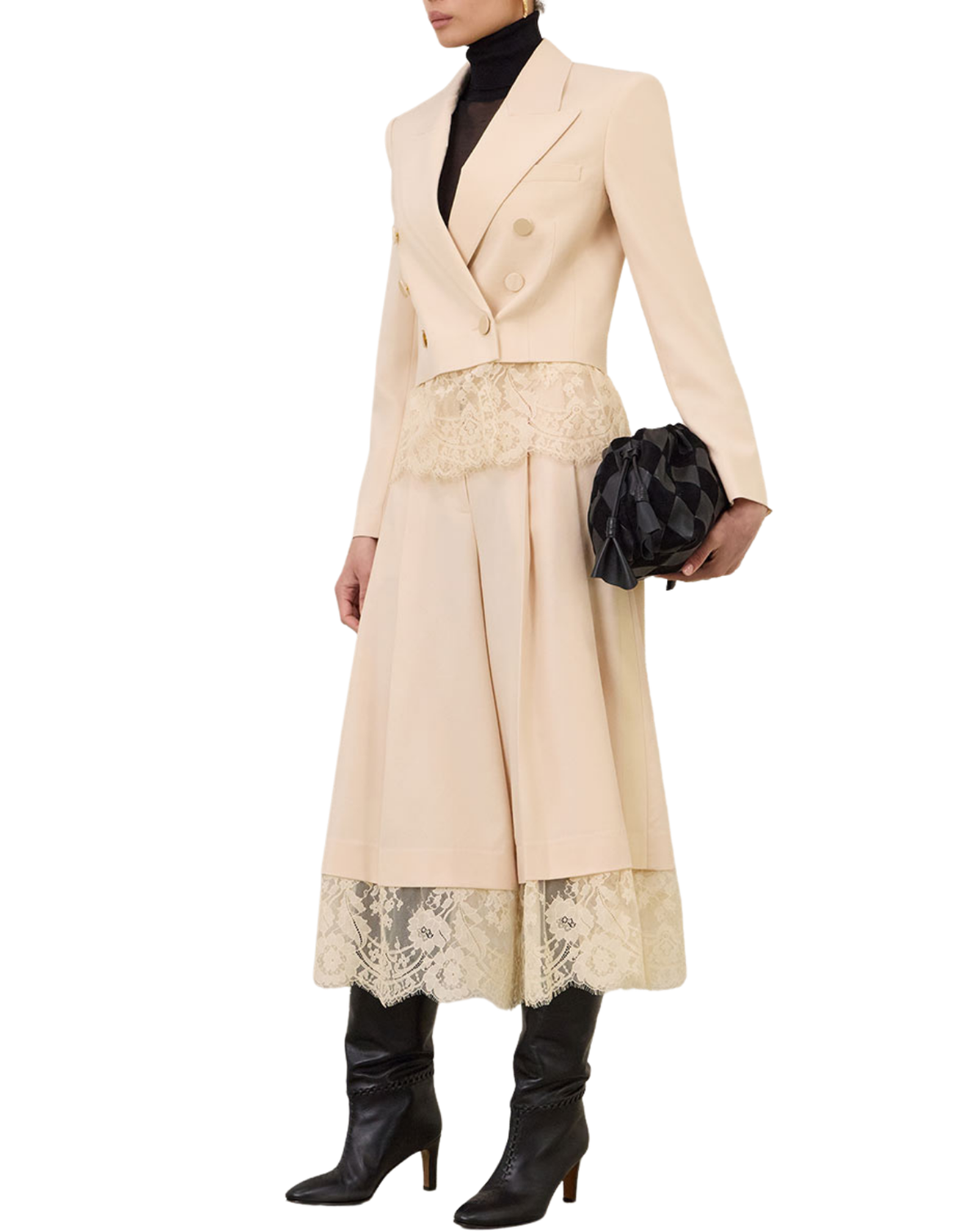 A model wears a beige double-breasted blazer with matching wide-leg trousers featuring a lace hem, styled with a black turtleneck, black knee-high boots, and a black patterned clutch bag against a white background.