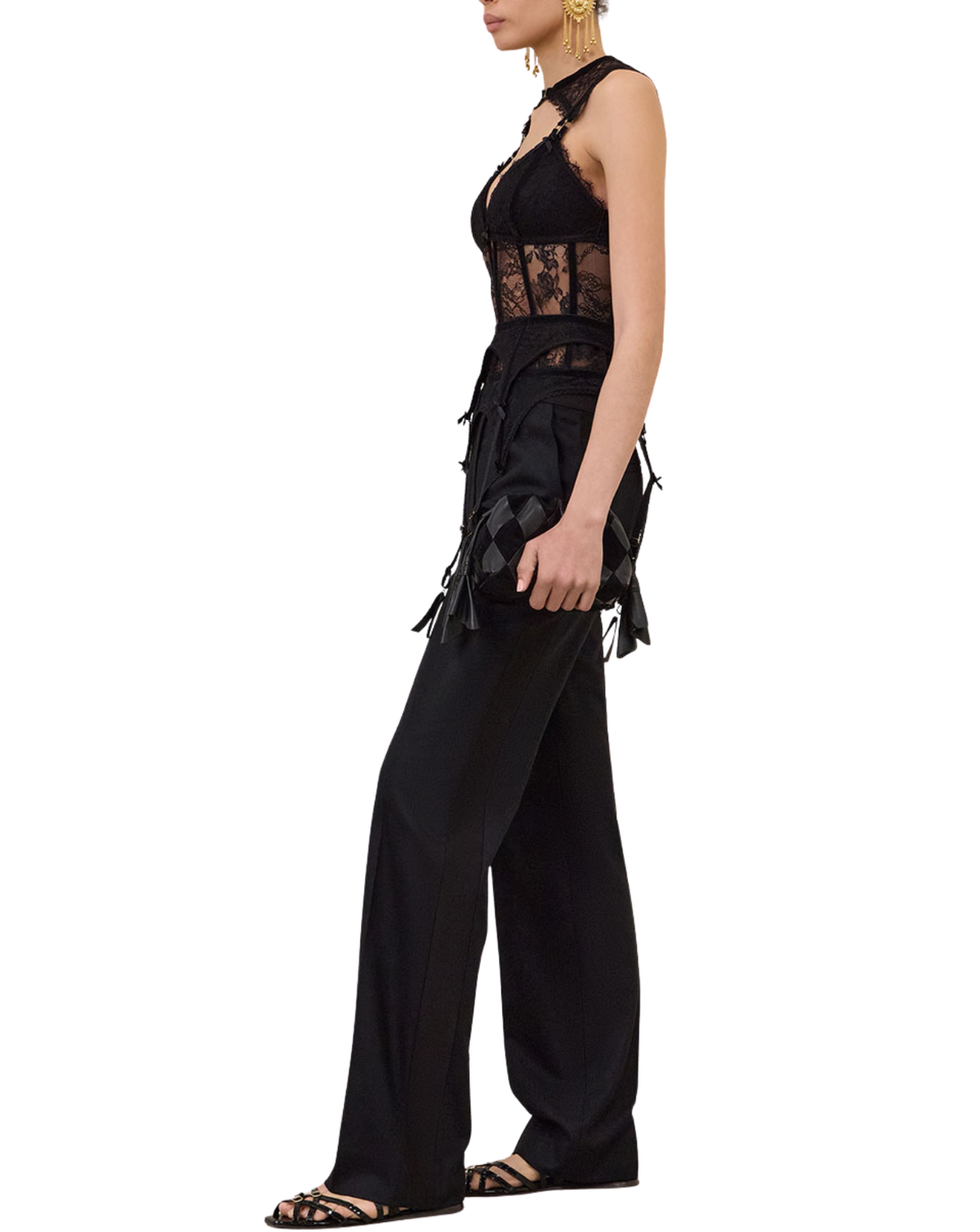 A model shown in profile wearing a black sleeveless lace-trimmed top and matching wide-leg pants with tassel details, photographed against a plain white background.