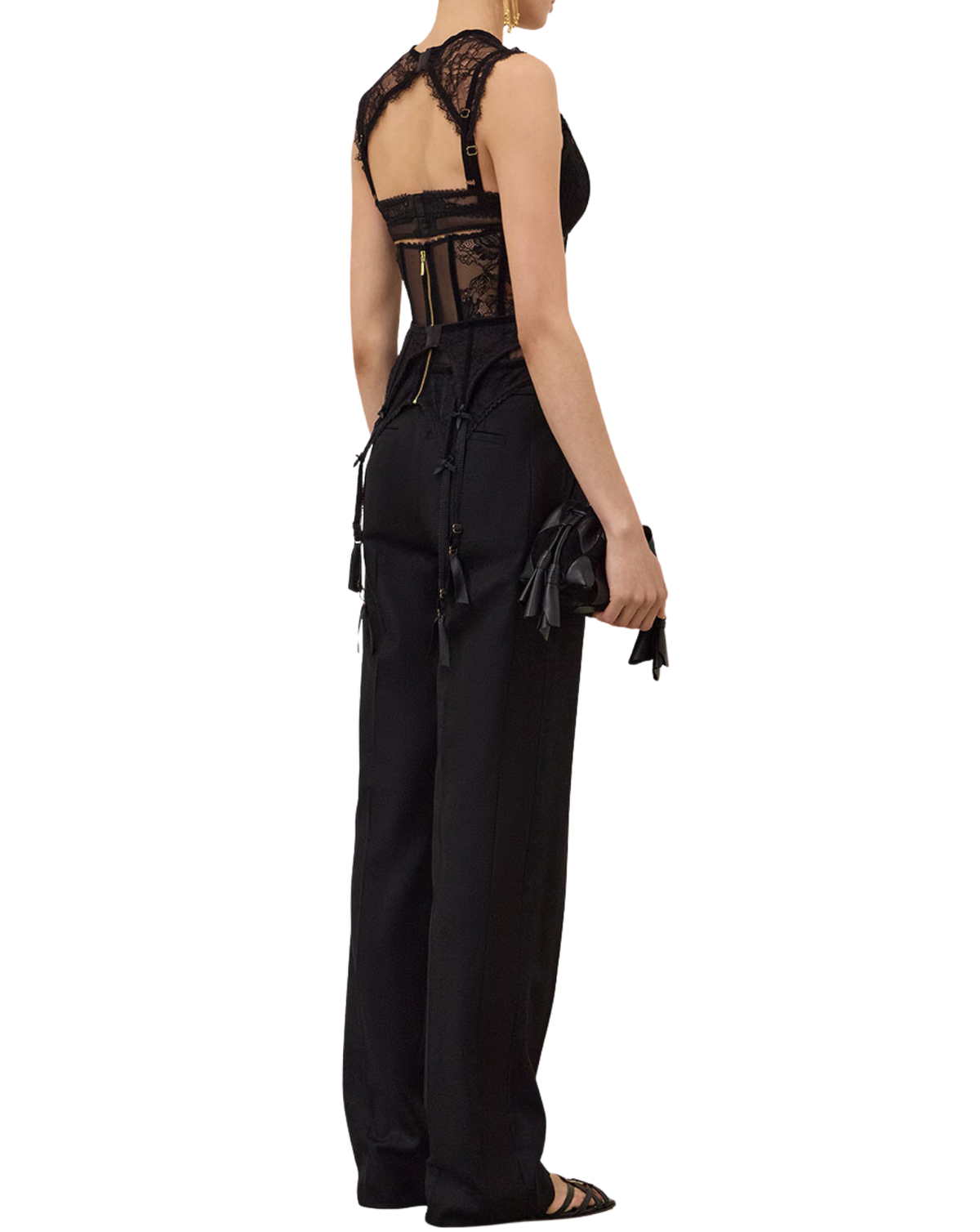 A model shown from the back wearing a black sleeveless lace-trimmed jumpsuit with wide legs and tie details at the back, paired with black strappy flat sandals against a plain white background.