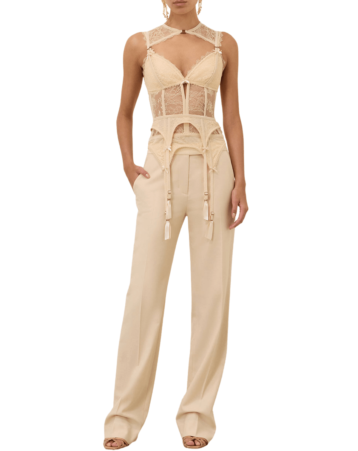 A model wearing a beige lace and satin jumpsuit with a halter-style neckline, sheer lace panels, and wide-leg trousers, shown against a plain white background.
