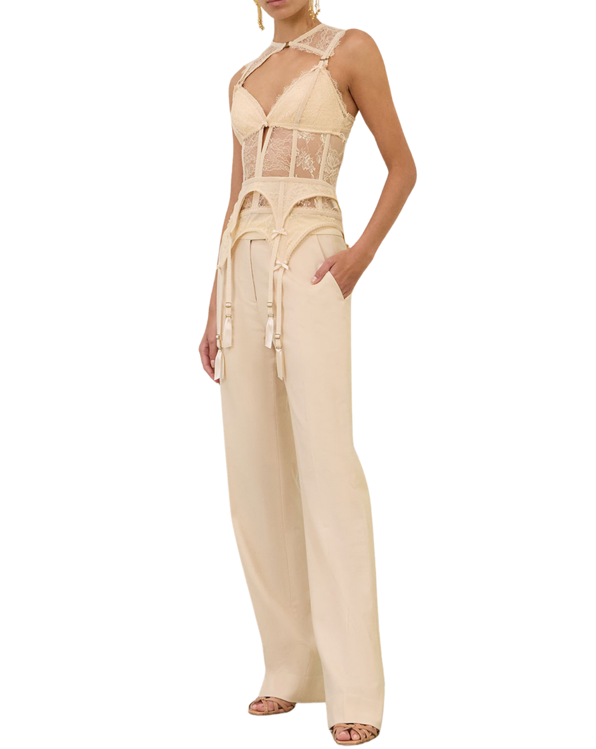 A model wearing a beige lace and mesh jumpsuit with wide-leg pants, a tie waist, and a halter-style neckline, shown against a plain white background.