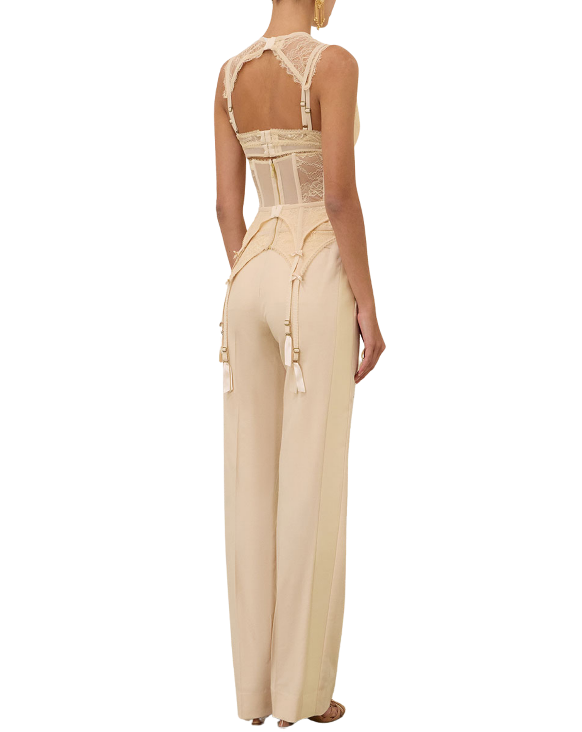A model shown from the back wearing a beige lace and satin jumpsuit with wide-leg trousers and suspenders, set against a plain white background.